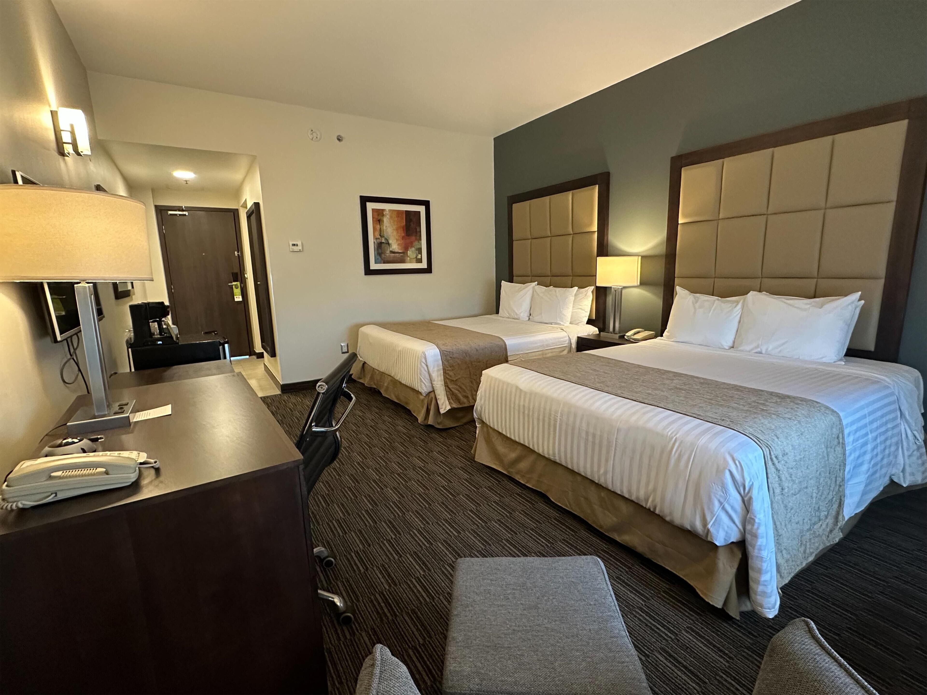 A hotel room with two beds, a desk with a telephone, a chair, and a painting on the wall.