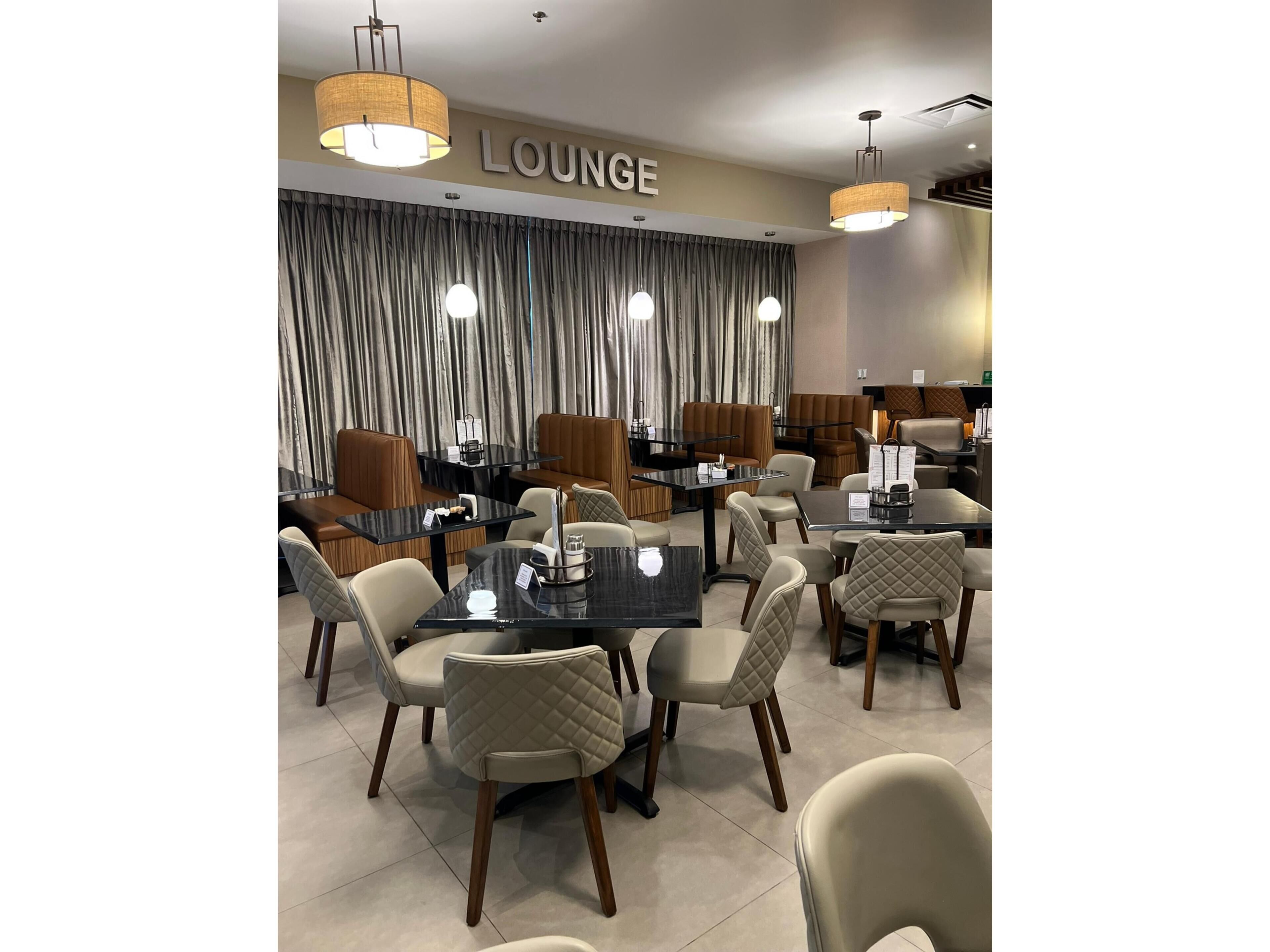 Un salón moderno con un letrero que dice 'LOUNGE', que cuenta con asientos de cuero, mesas de vidrio e iluminación colgante.