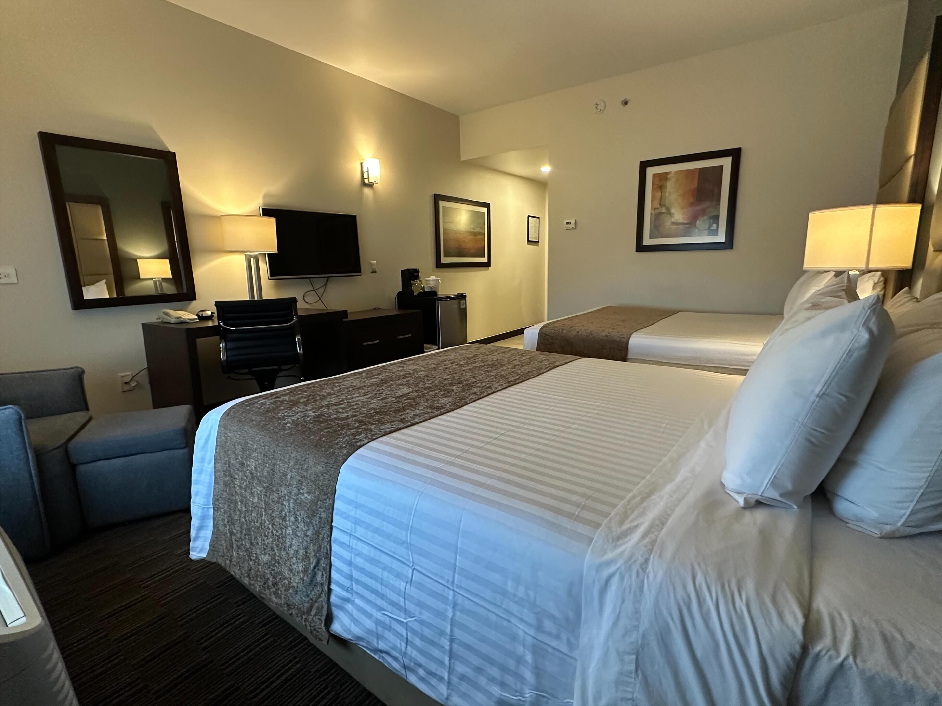Habitación de hotel con dos camas, un escritorio, una silla, un televisor y un cuadro en la pared.