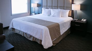 Habitación de hotel con una cama grande, dos lámparas de noche, una mesita con teléfono y una ventana que deja entrar luz natural.