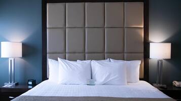 A hotel room with a large bed, two bedside lamps, a nightstand, a clock, and a bedside table with a phone.