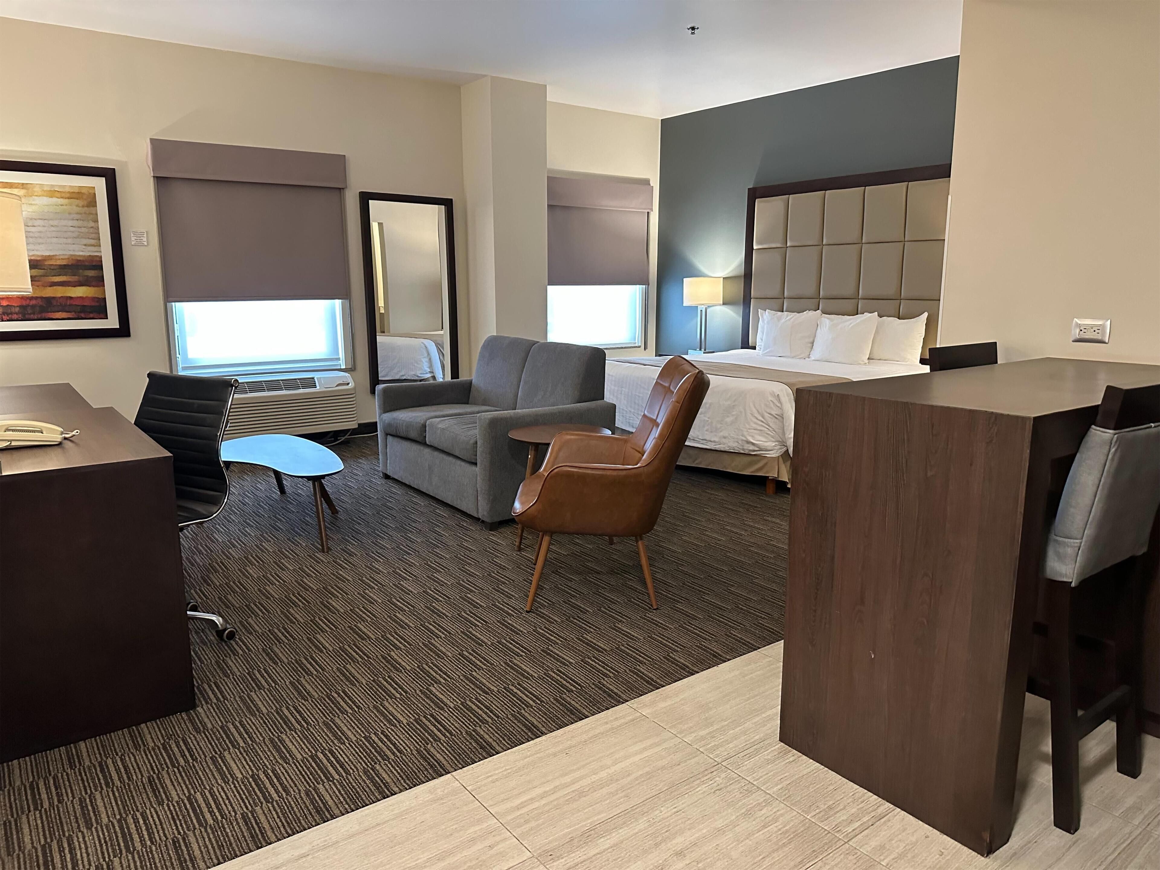 Una habitación de hotel con una cama, un escritorio, una silla, una mesita y un espejo grande.