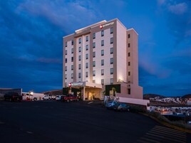 Un hotel de varios pisos con fachada plana, un letrero destacado que dice "Best Western PLUS", y un estacionamiento con varios vehículos.