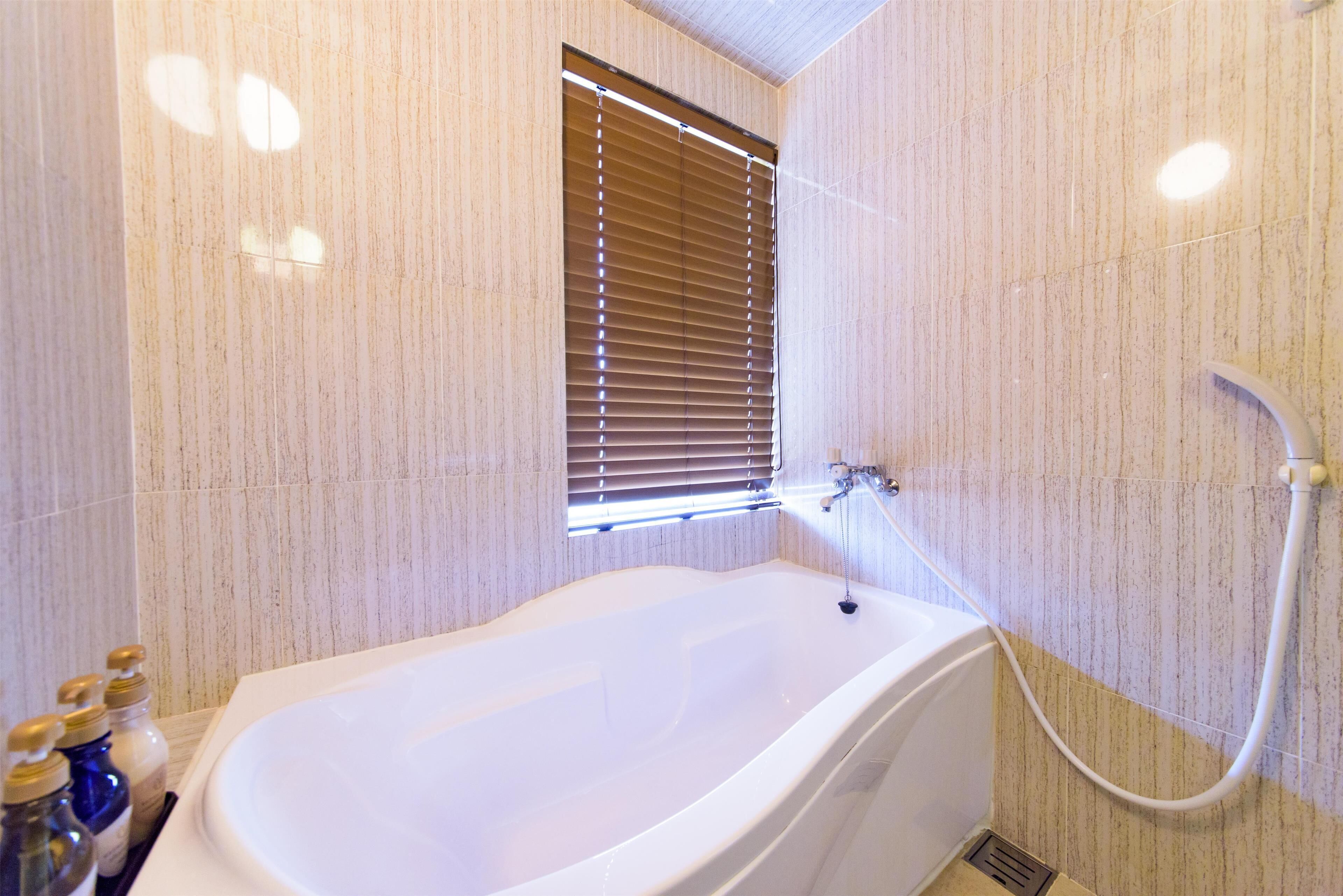 A bathroom with a freestanding bathtub, a window with blinds, and a shower area.