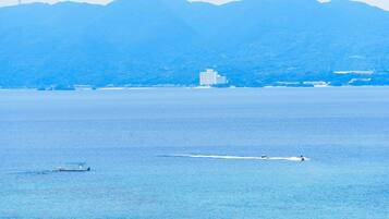 Una masa de agua tranquila con un bote y un jet ski. En el fondo, se observa un edificio grande y una colina.