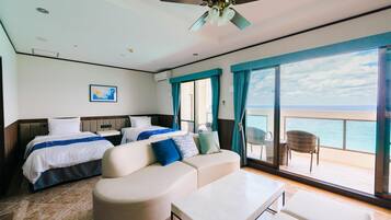 A hotel room with a bed, a sofa, a dining table, and a view of the ocean.