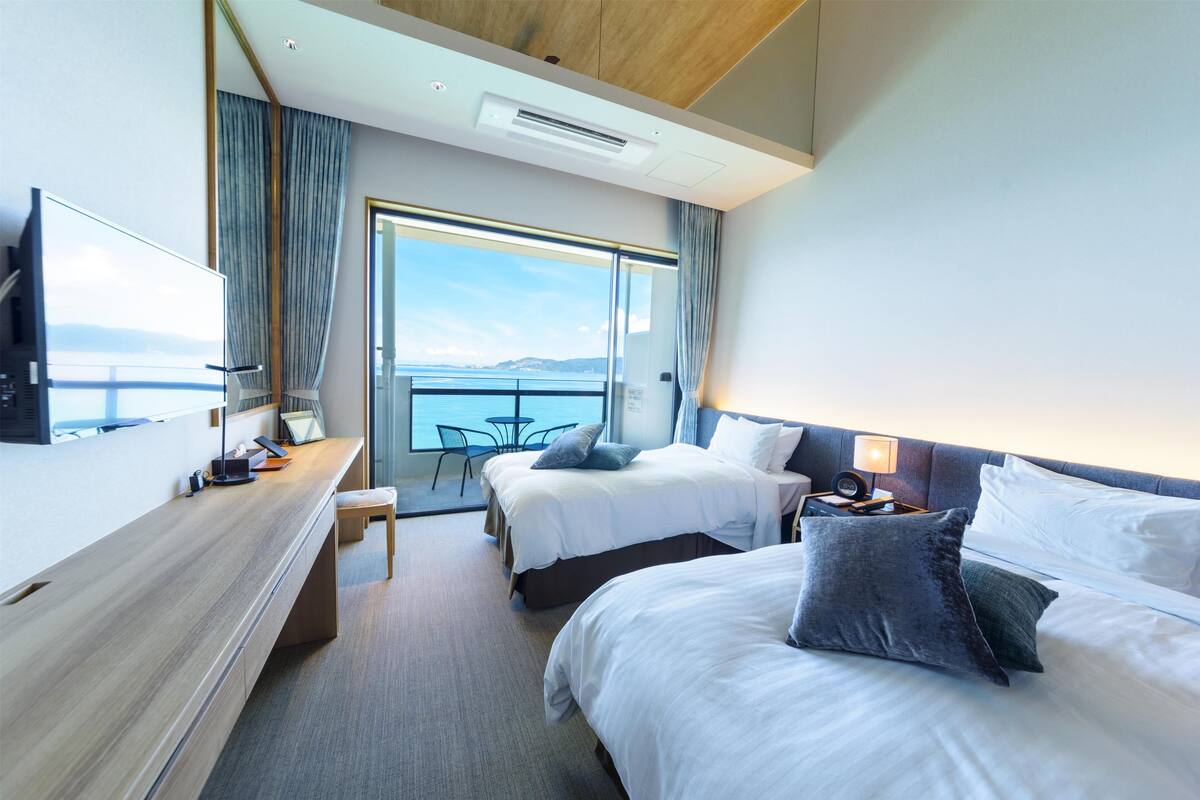 Een moderne hotelkamer met twee bedden, een bureau en een groot raam met uitzicht op zee.