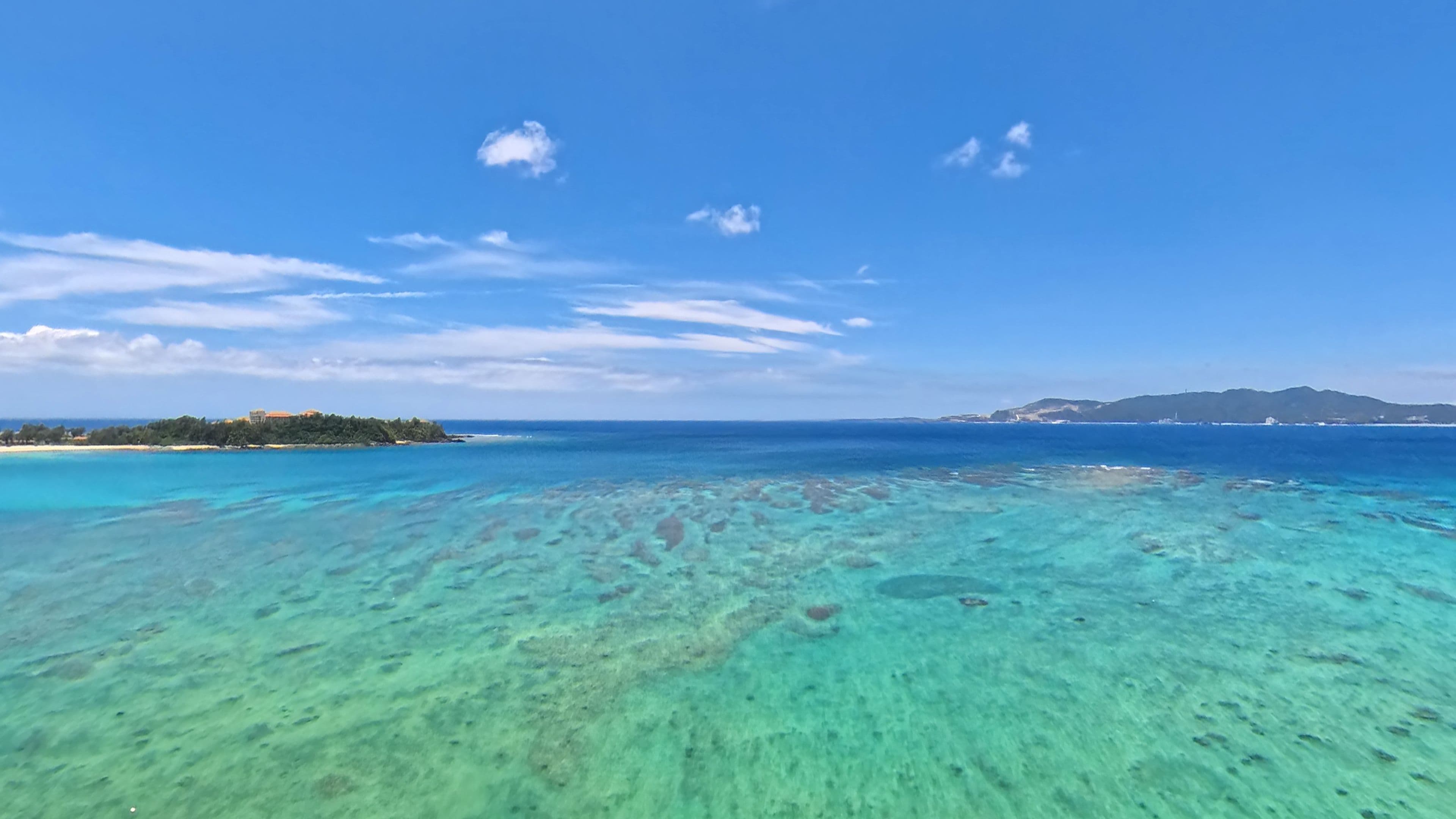 A clear view of a tropical beach with shallow waters and a distant island.