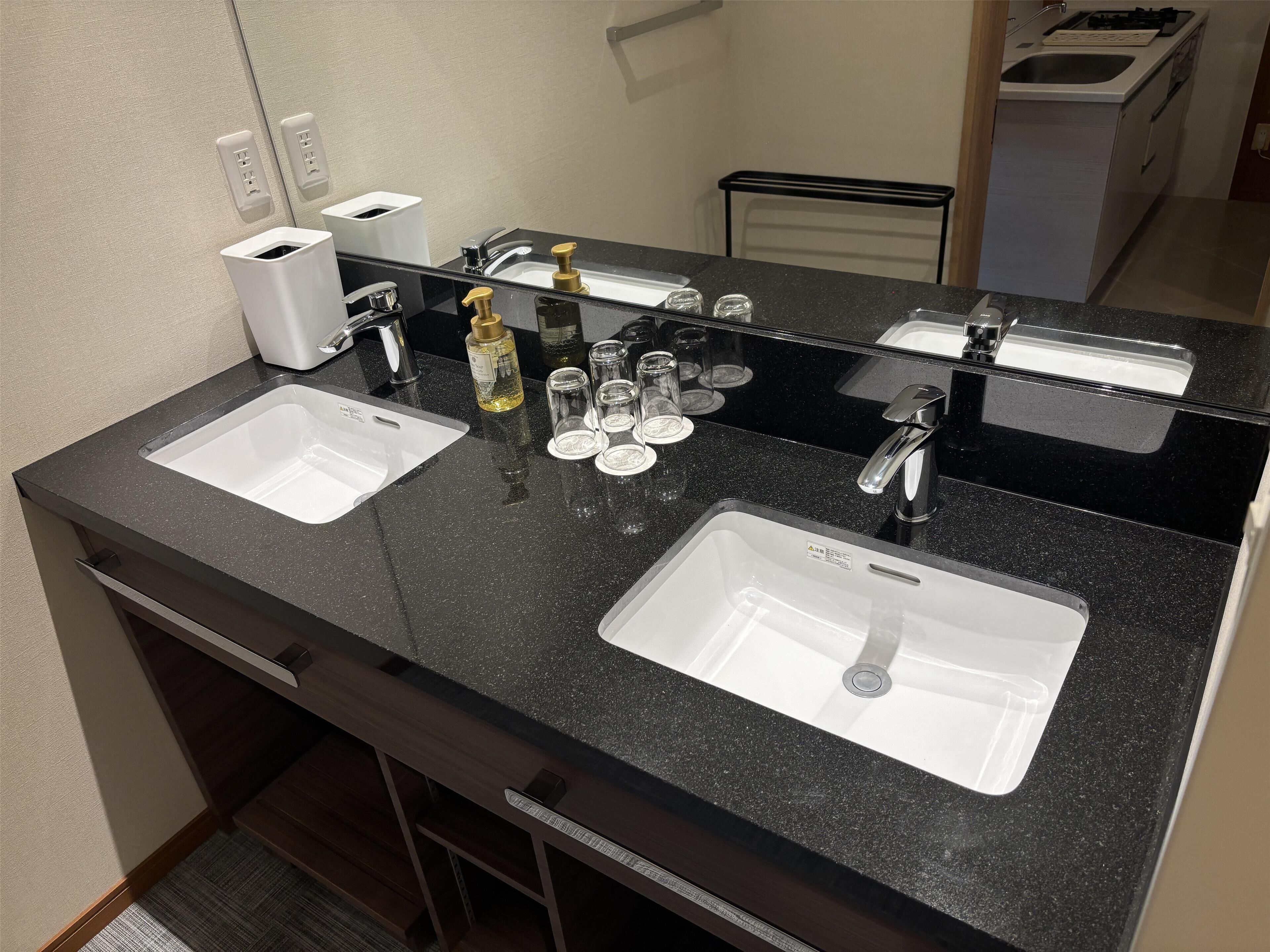 A modern bathroom with two sinks, a mirror, and a countertop with toiletries.