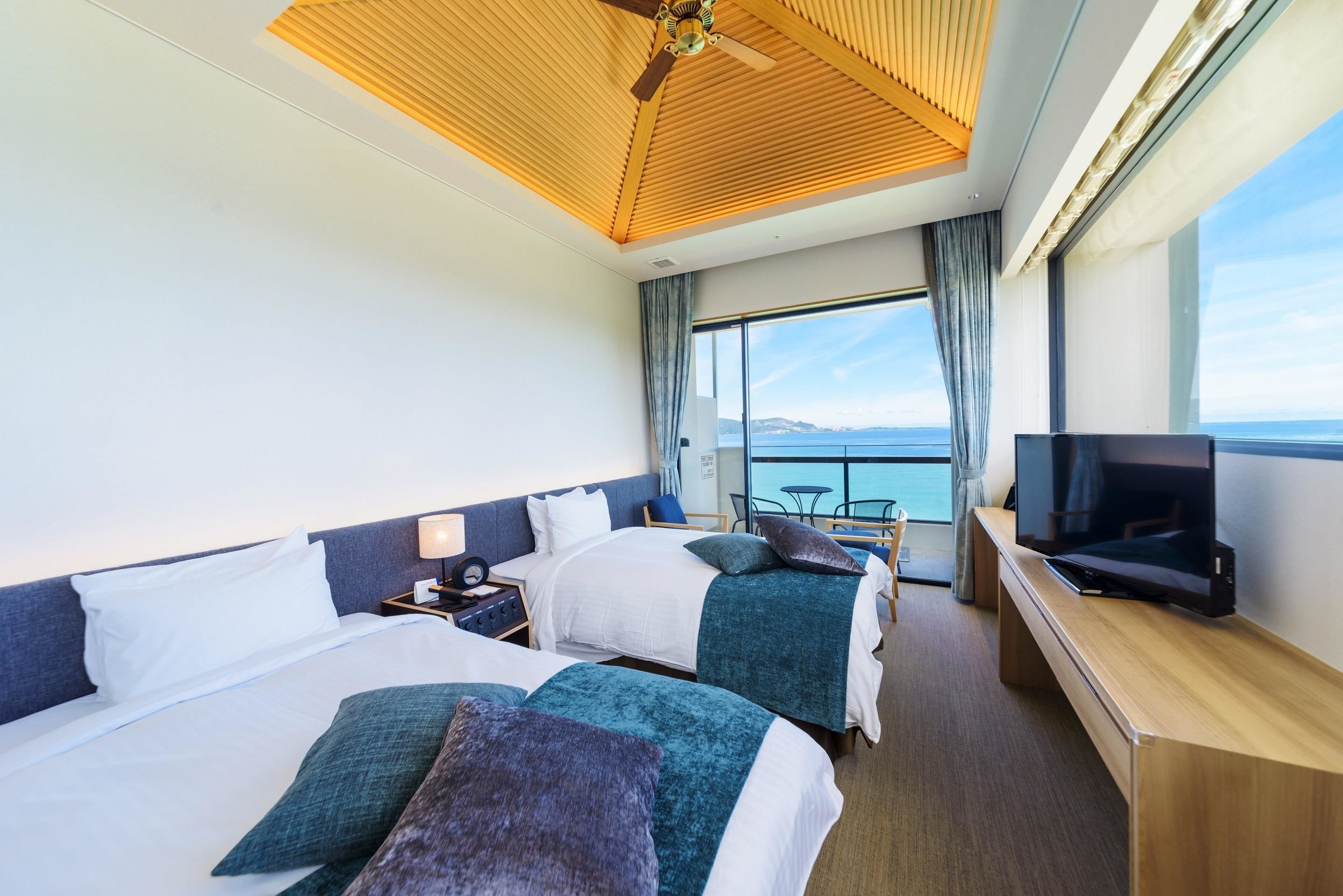 Ett hotellrum med två sängar, en TV, ett träpanelat tak och utsikt över havet.