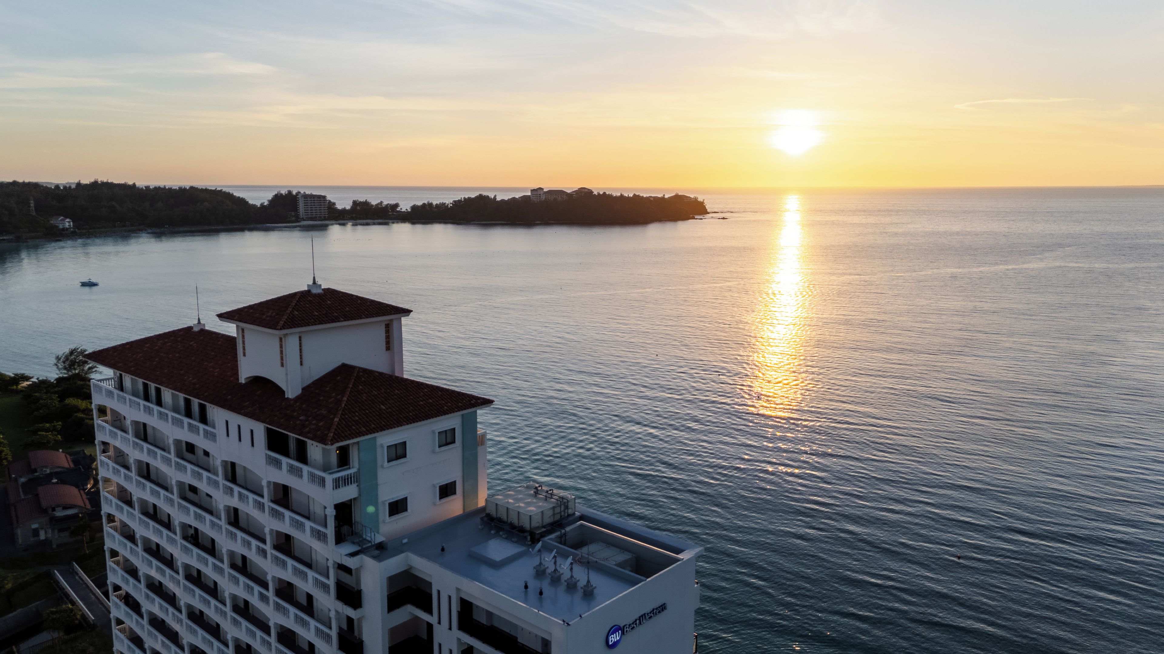 Un hotel moderno con terraza en la azotea y vistas a un cuerpo de agua al atardecer.