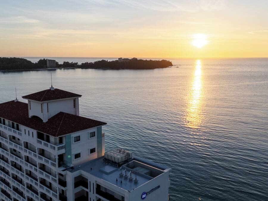Un hotel moderno con terraza en la azotea y vistas a un cuerpo de agua al atardecer.