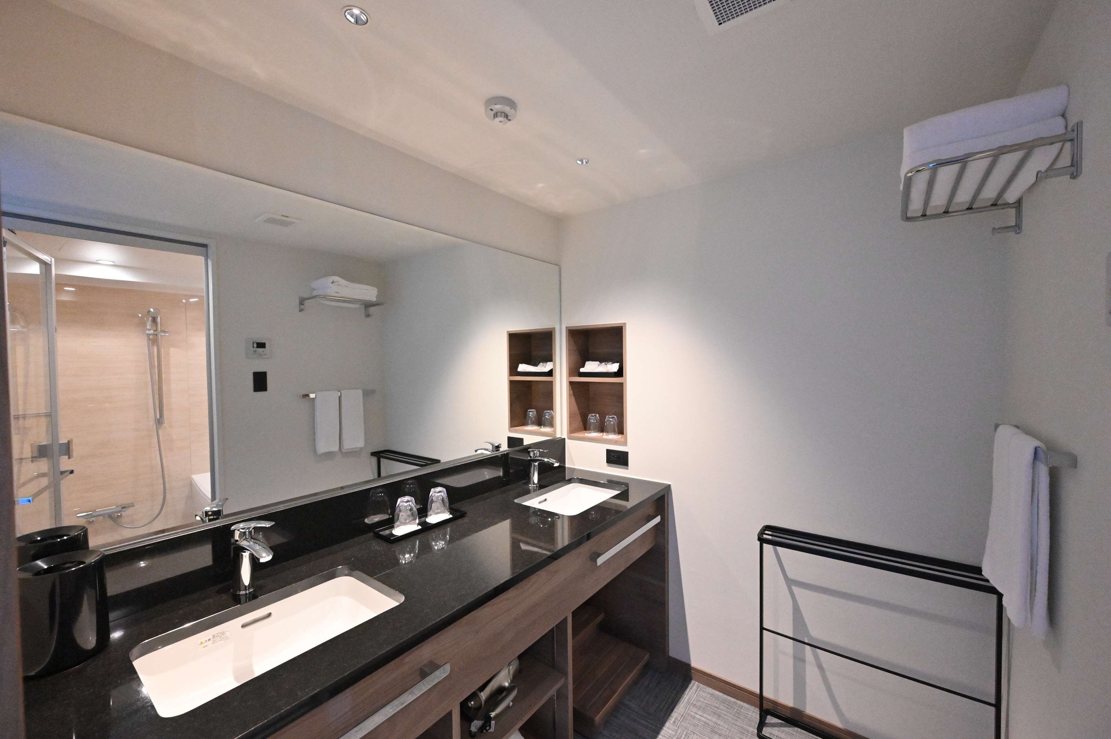 A modern bathroom with a large mirror, two sinks, a shower, and a towel rack.