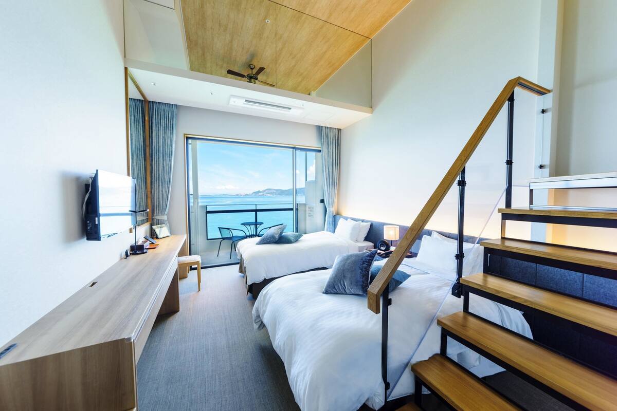 Een moderne hotelkamer met twee bedden, een bureau en uitzicht op zee.