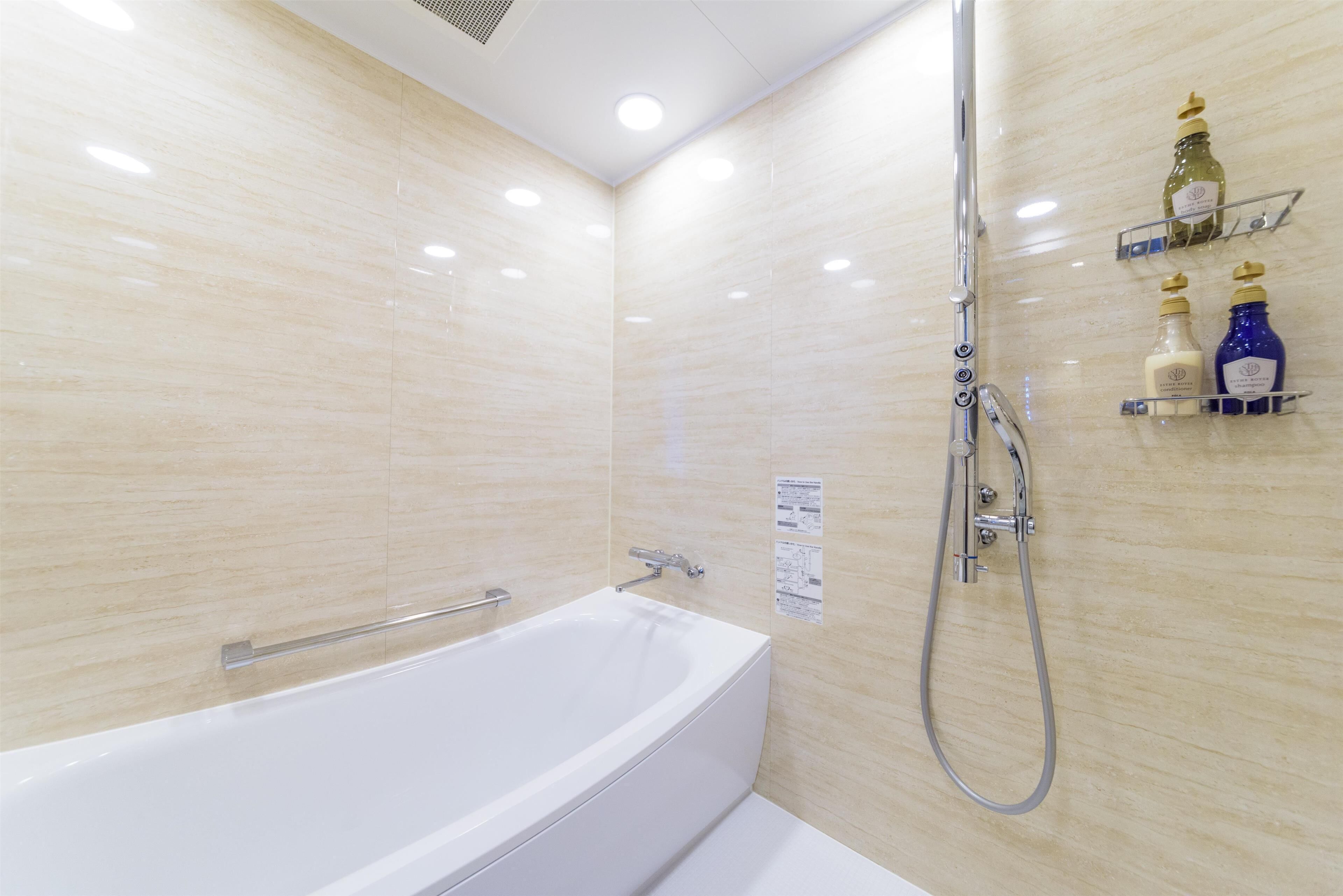 Un baño moderno con una bañera blanca, ducha con cabezal de mano y estantes con artículos de aseo.