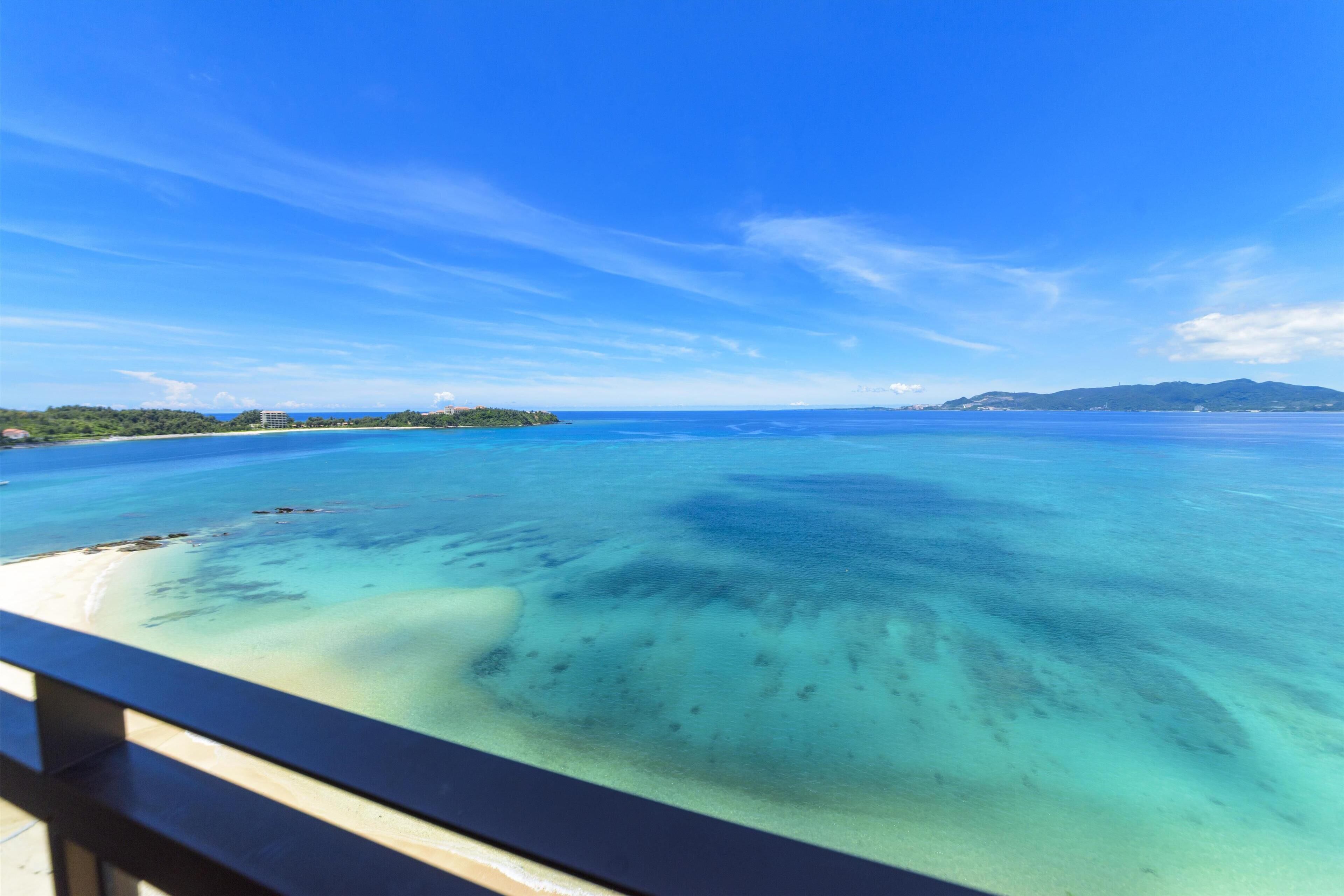 A coastal view with clear turquoise waters, a sandy beach, and distant hills.