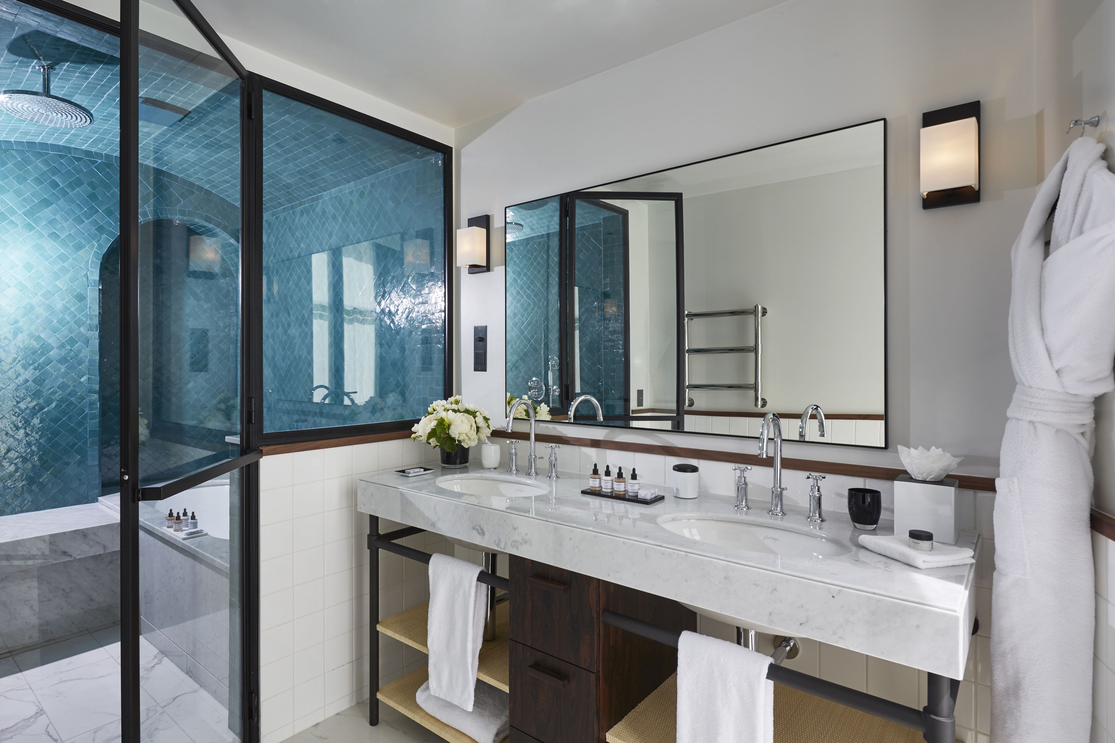 A modern bathroom with a large mirror, two sinks, and a glass-enclosed shower area.