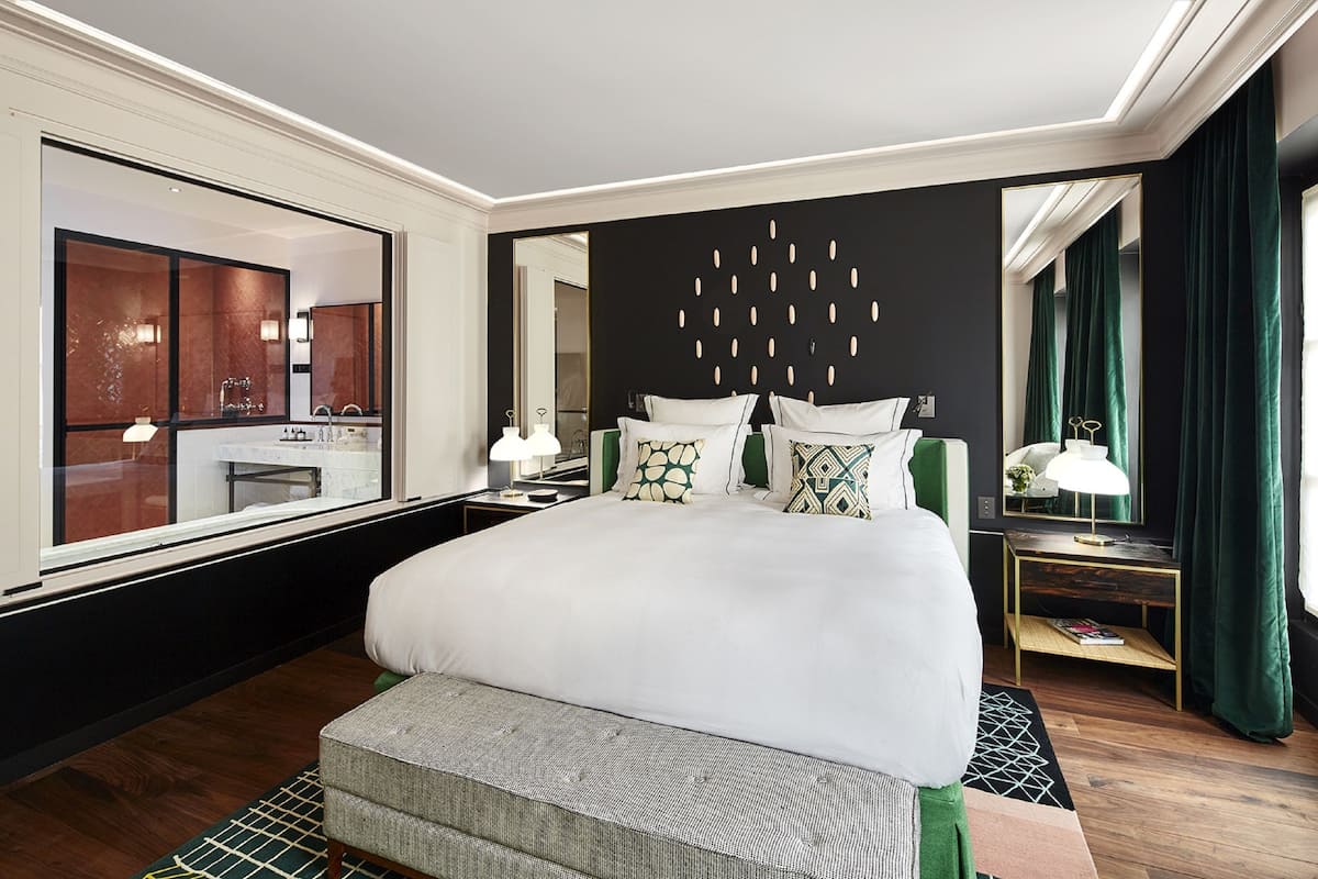 A hotel room with a large bed, two bedside tables, a mirror, and a view of the bathroom.
