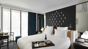 Une chambre d’hôtel avec un grand lit, une table de chevet avec une lampe, un bureau avec une chaise et une fenêtre avec des rideaux.