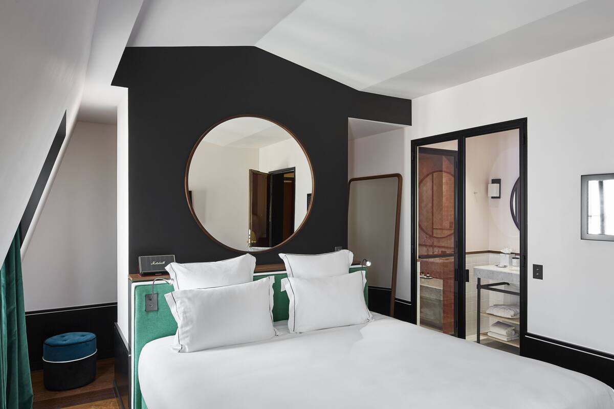 A modern hotel room with a large bed, a round mirror, a green accent wall, and a visible bathroom.