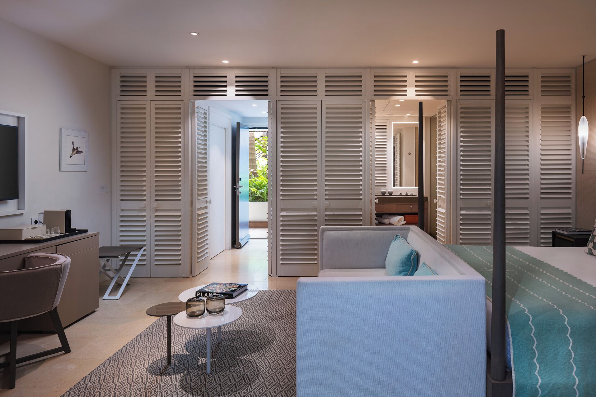 A modern hotel room with a sofa, a small table, a TV, and a wardrobe with sliding doors.
