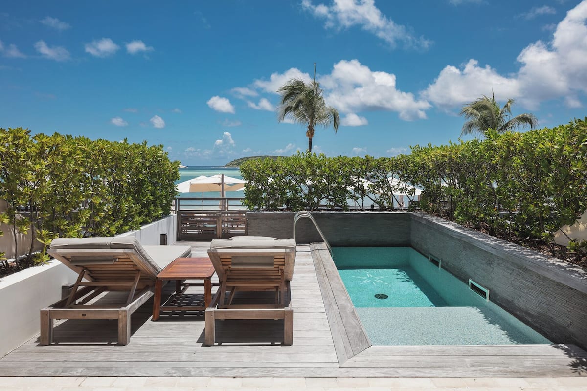 A pool area with wooden loungers, a small table, and umbrellas.