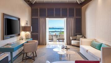 A modern hotel room with a flat-screen TV, a desk, a sofa, and a balcony with a view of the sea.