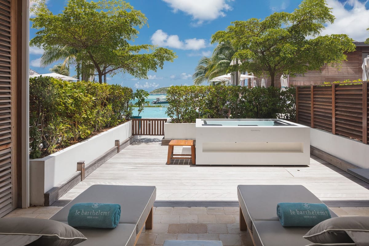 A rooftop pool area with lounge chairs, a hot tub, and a view of the ocean.