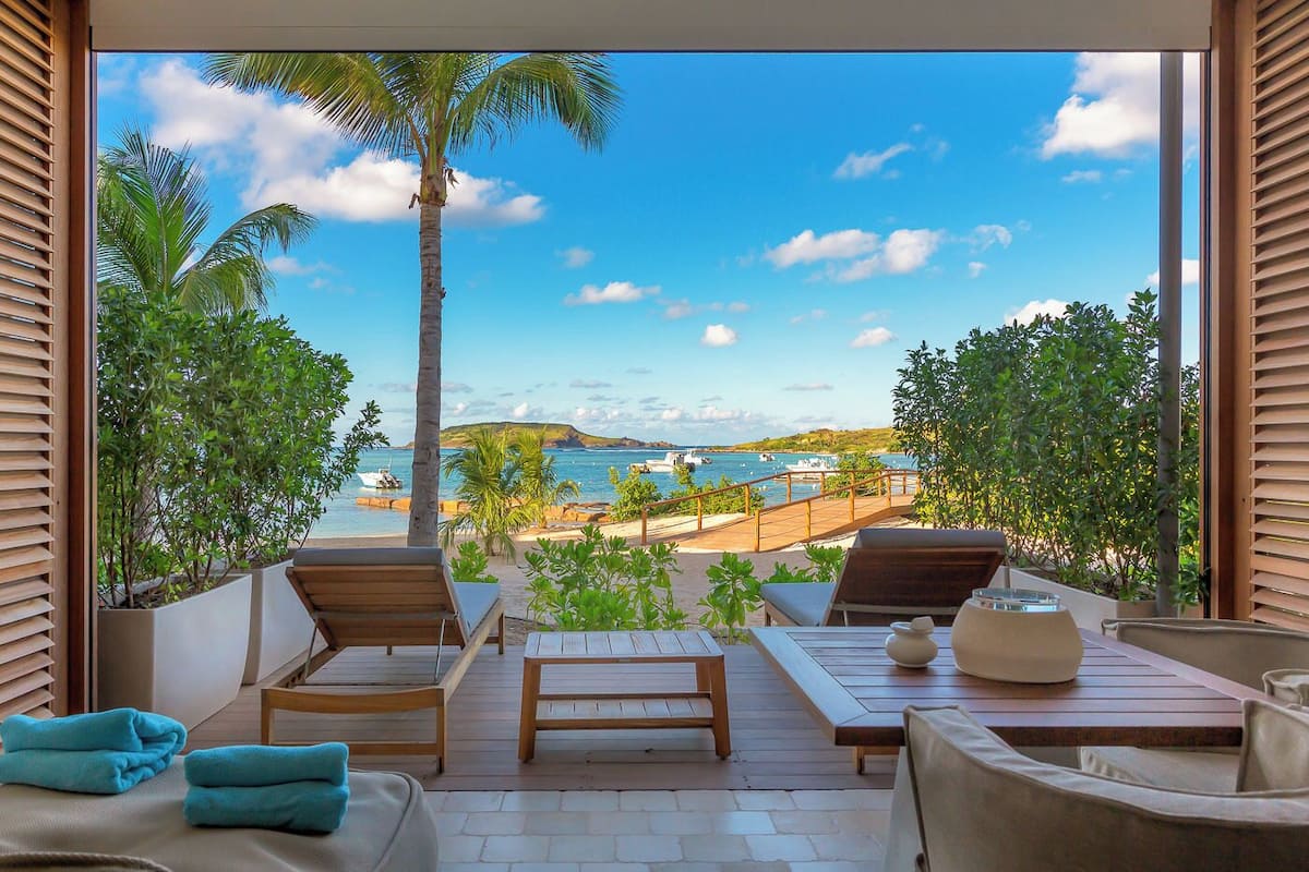A balcony with wooden furniture, a view of the sea, and a palm tree.