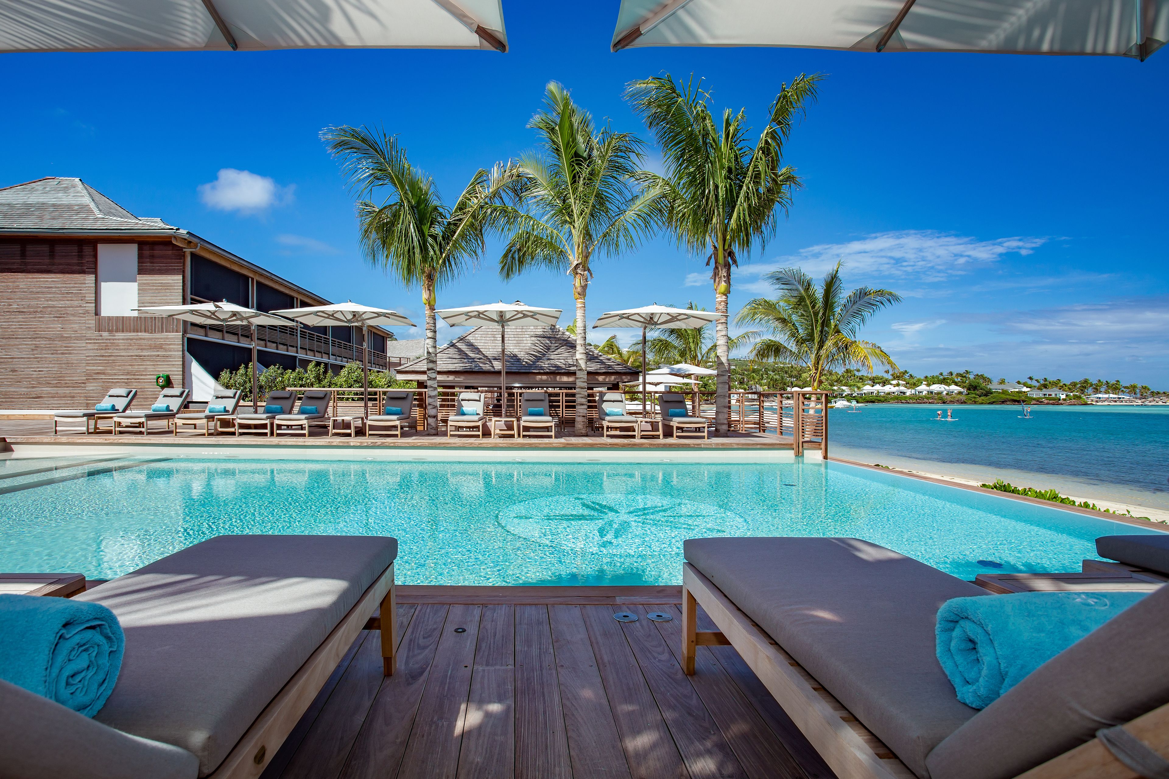 A poolside area with lounge chairs and umbrellas, a wooden deck, and a view of the ocean.