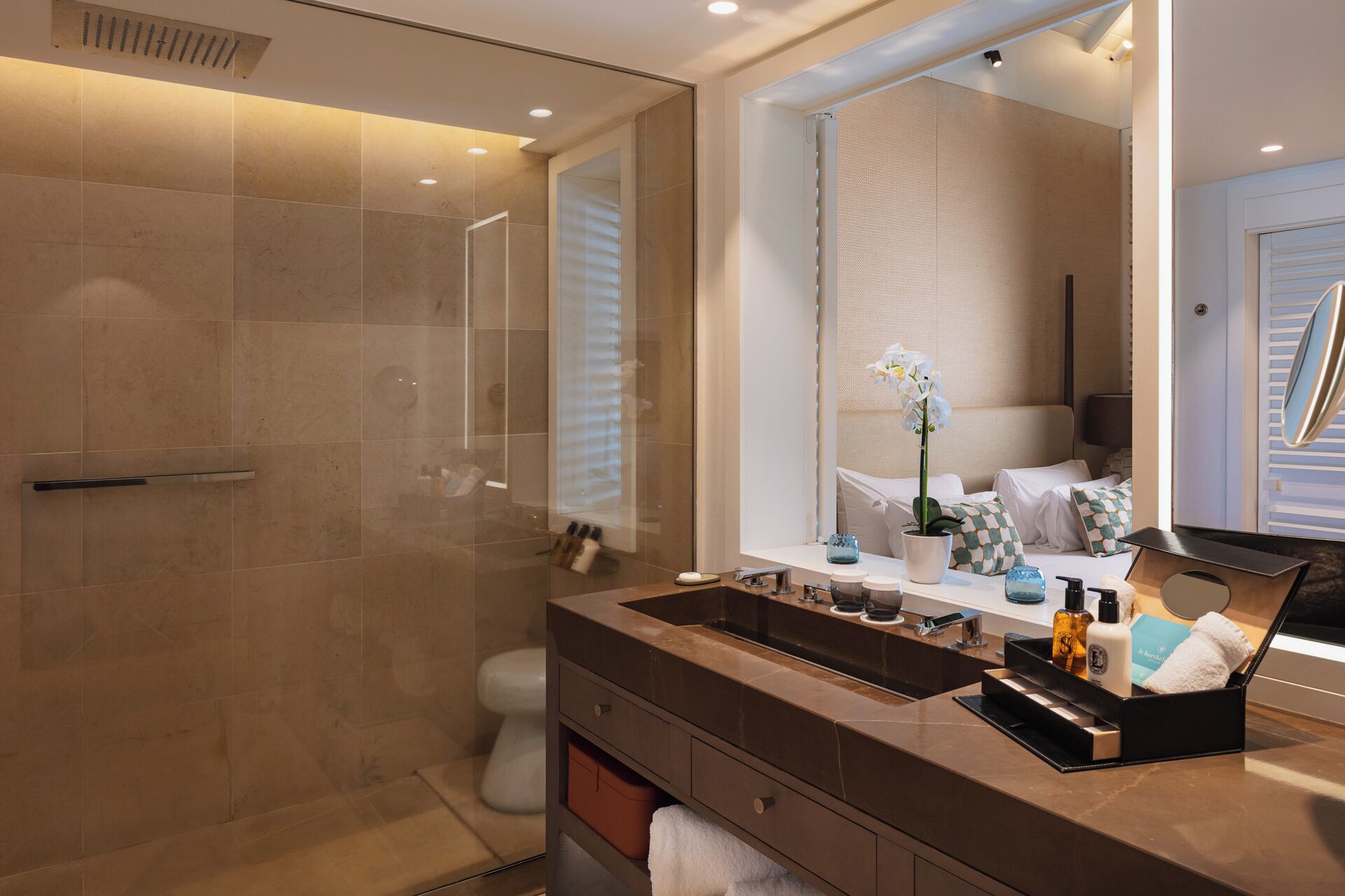 A modern bathroom with a glass-enclosed shower, a large mirror, and a vanity with a sink and multiple toiletries.