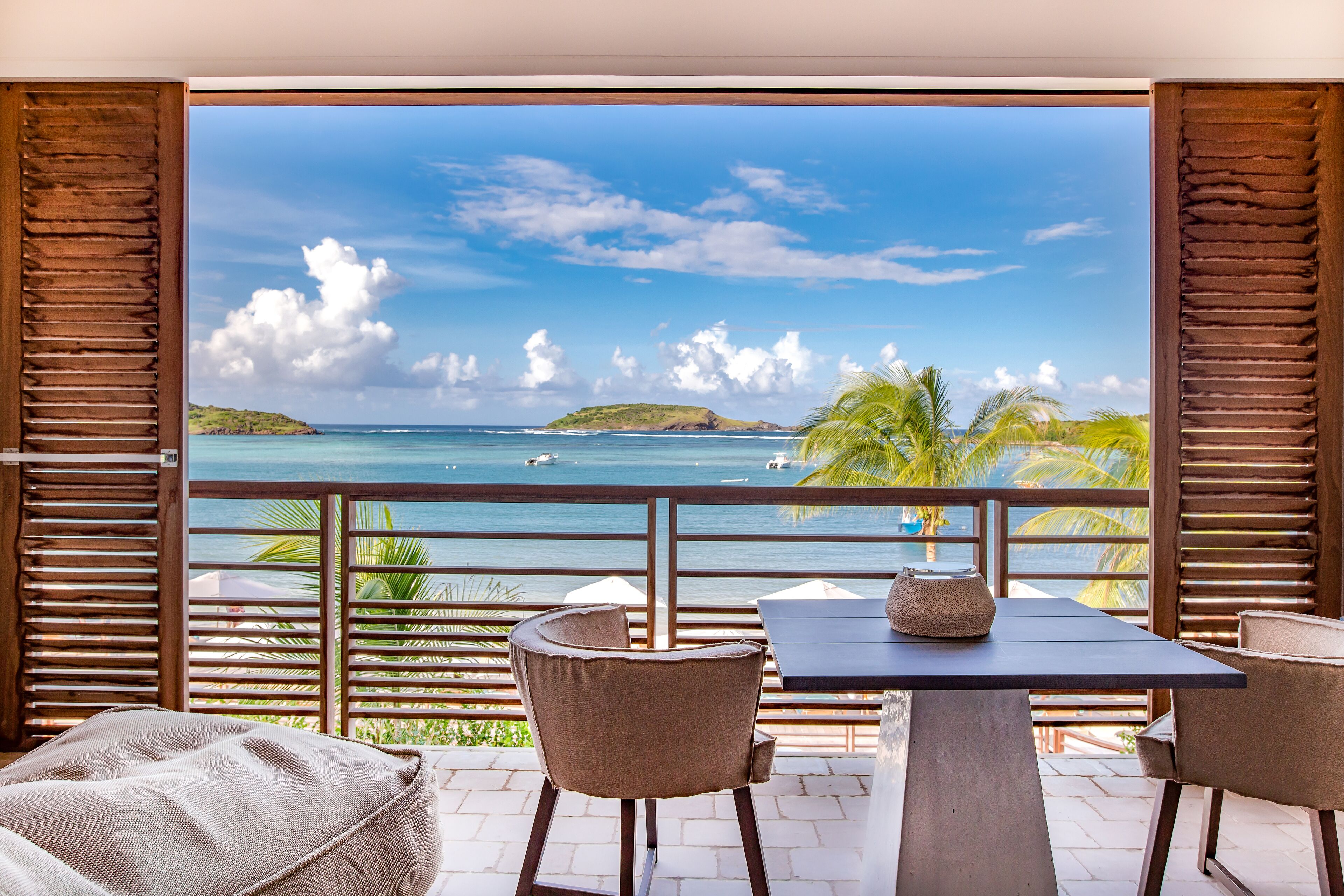 A balcony with a view of the ocean, wooden railings, and two chairs.