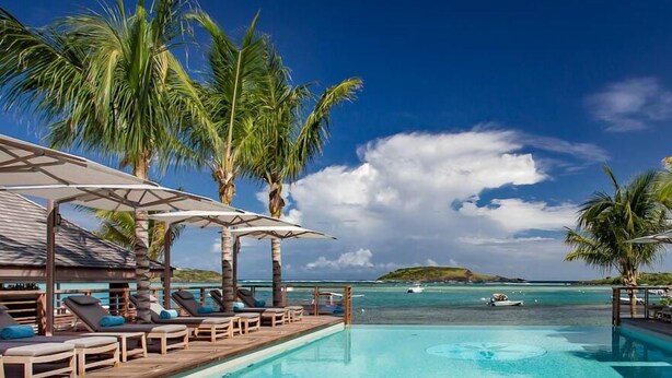 A clear blue pool with lounge chairs and umbrellas, surrounded by palm trees and a view of the ocean. - Le Barthélemy Hotel & Spa (St. Barthelemy)