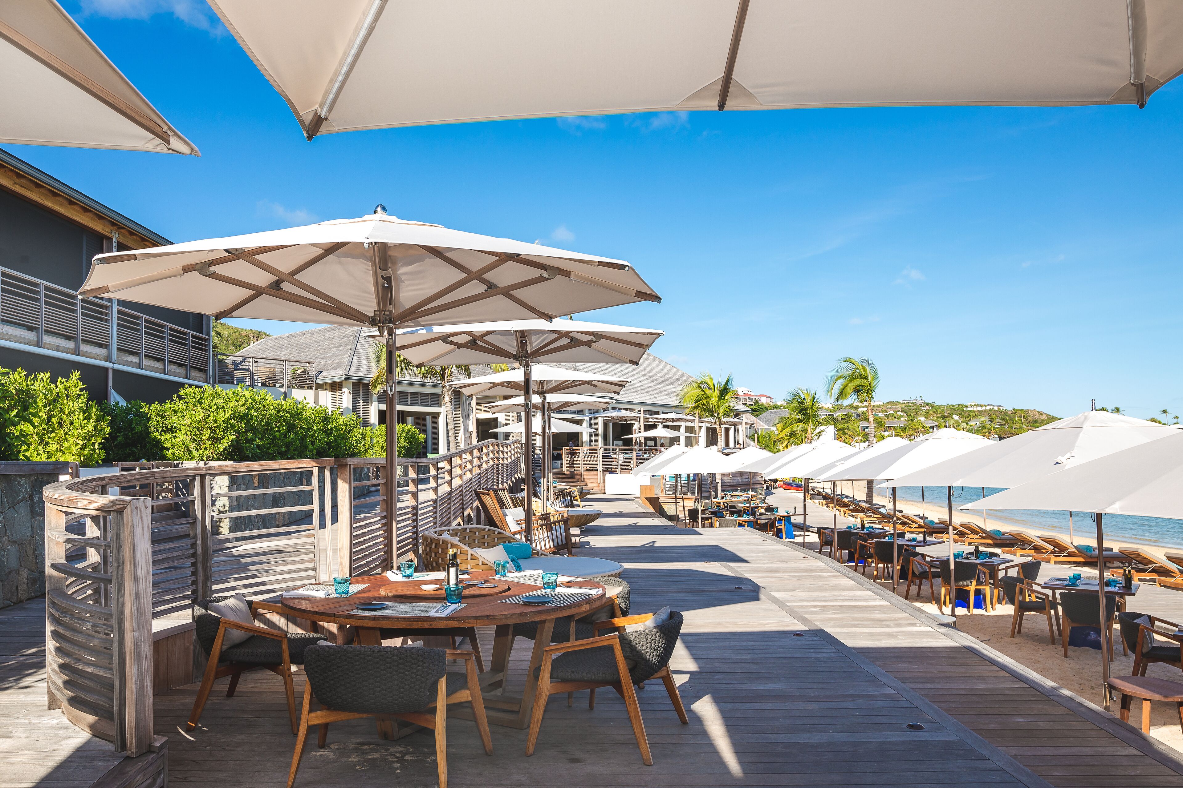 Un restaurant en bord de mer avec une terrasse, des parasols blancs et une plateforme en bois.