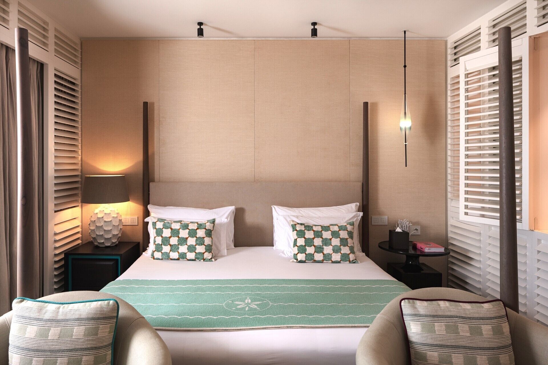 Habitación de hotel con una cama grande, dos mesitas de noche, una manta verde y vistas al exterior a través de la ventana.