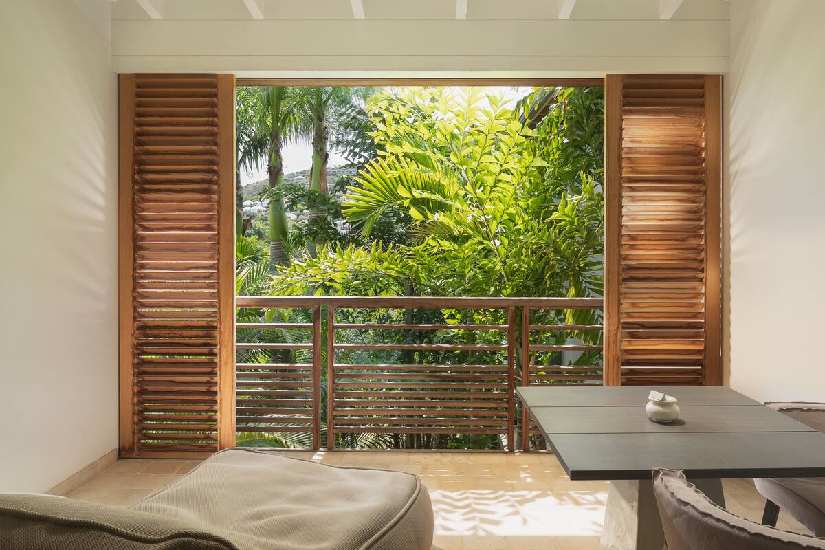 A balcony with wooden shutters, a table, and a cushioned seating area.