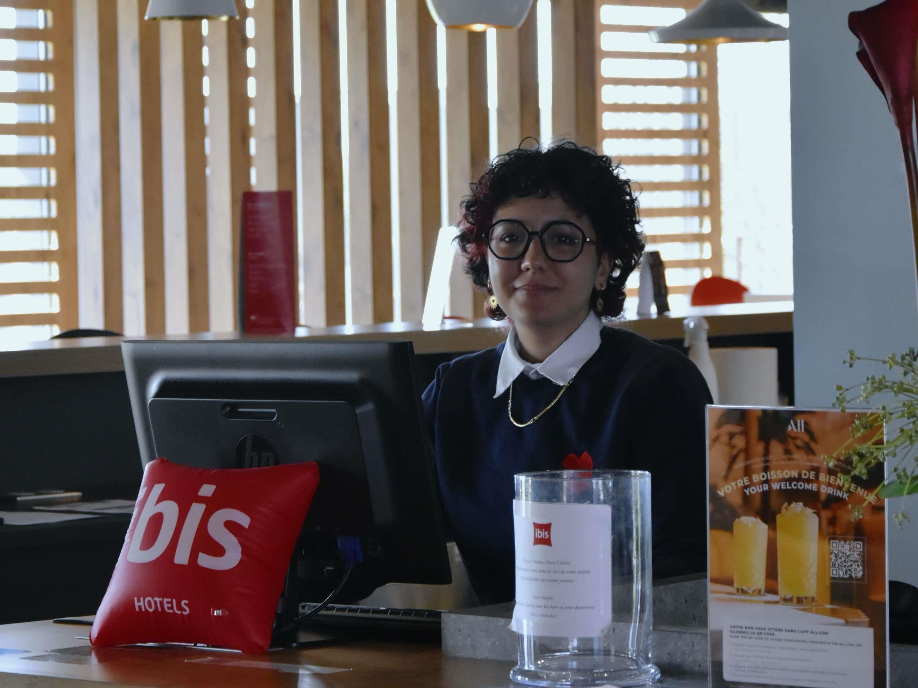 A hotel reception desk with a red 'bIs' bag, a glass with a label, and a brochure.
