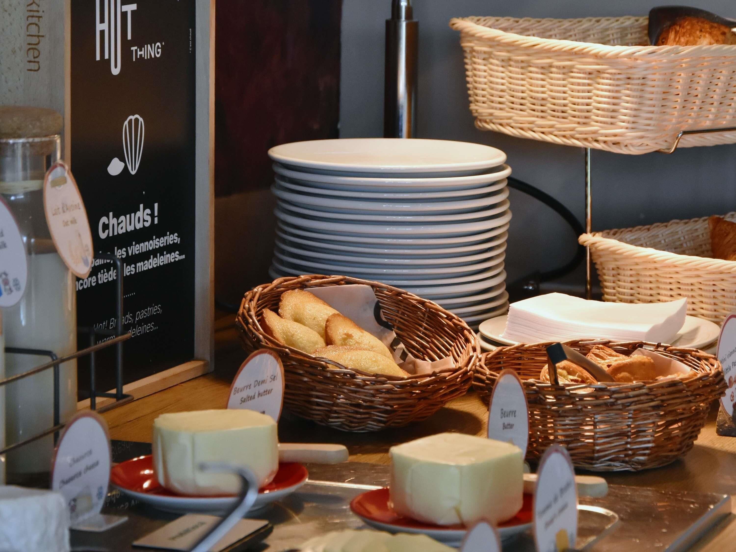 A buffet setup with various cheeses, bread, and stacked plates.