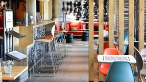 Een modern café met metalen stoelen, houten tafels en een rode bank.