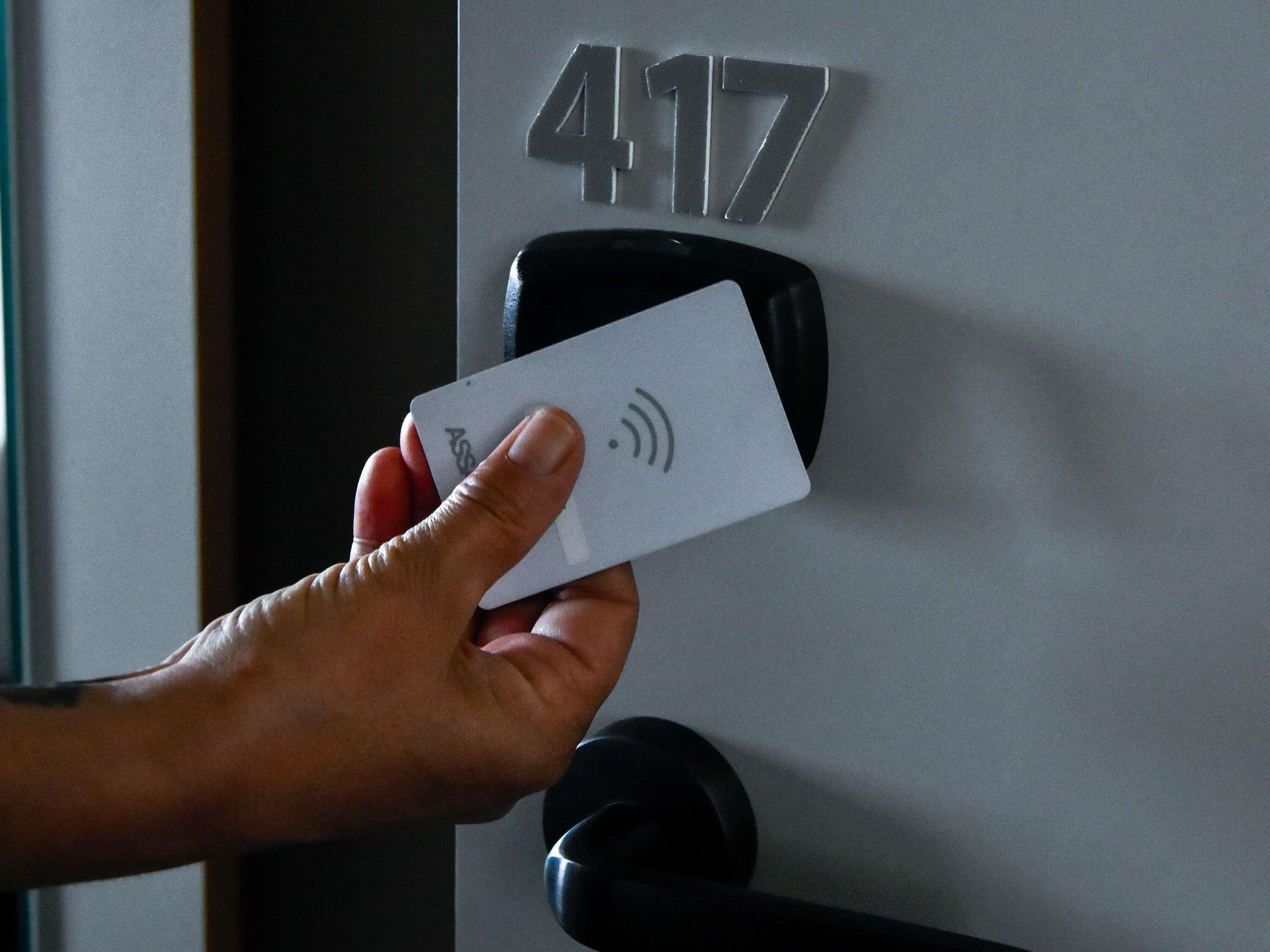A hand holding a card with a Wi-Fi symbol, near a door with the number 417 and a black intercom.