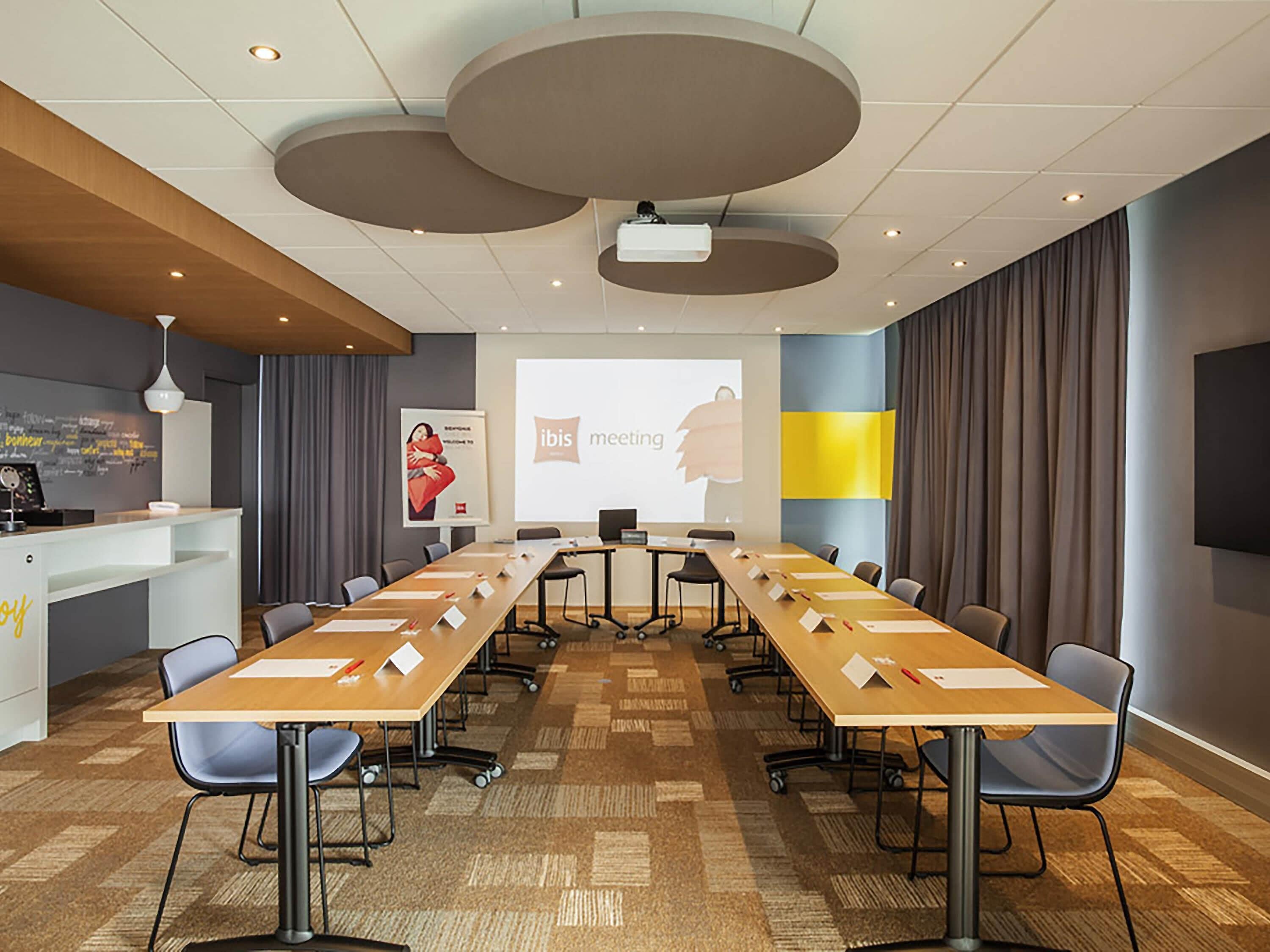 A conference room with a long table, chairs, a projector screen, and a presentation on the wall.