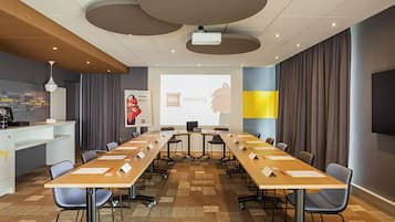 A conference room with a long table, chairs, a projector screen, and a presentation on the wall.