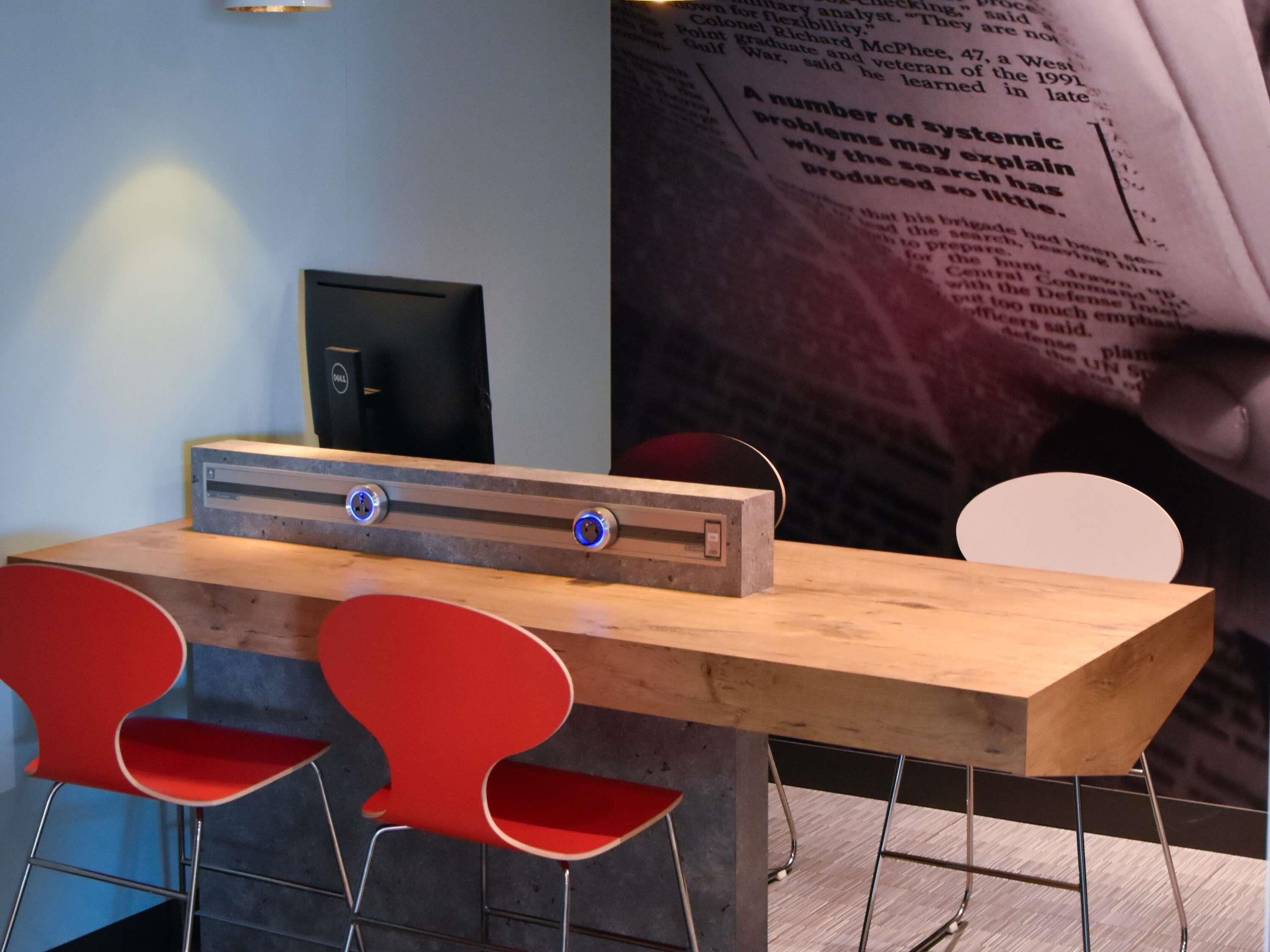 A modern conference room with a wooden table, two red chairs, and a black speaker.