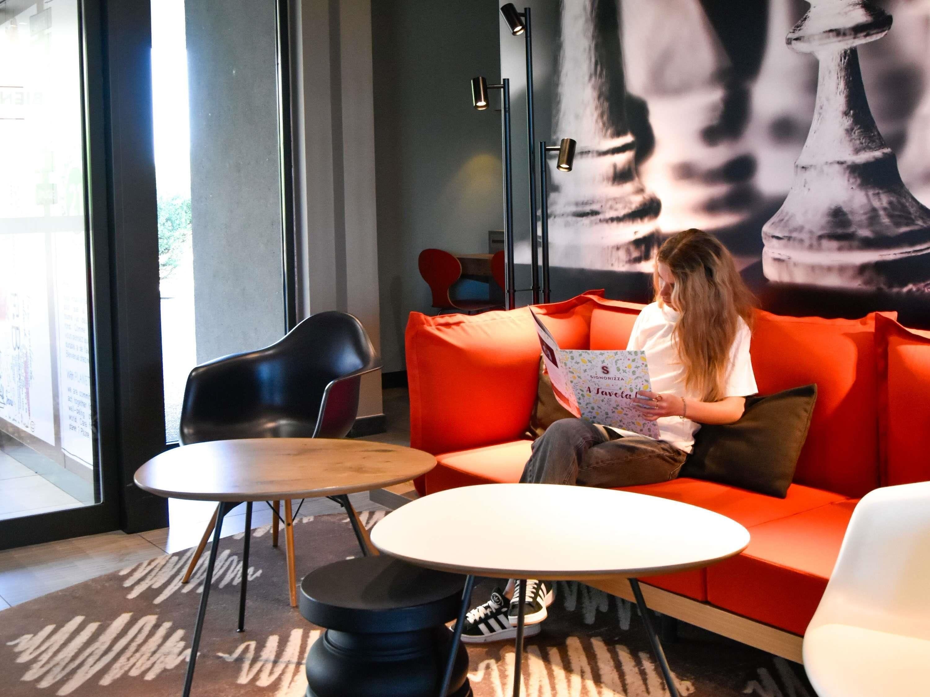 A person reading a book on a red couch with a large chess piece mural in the background.