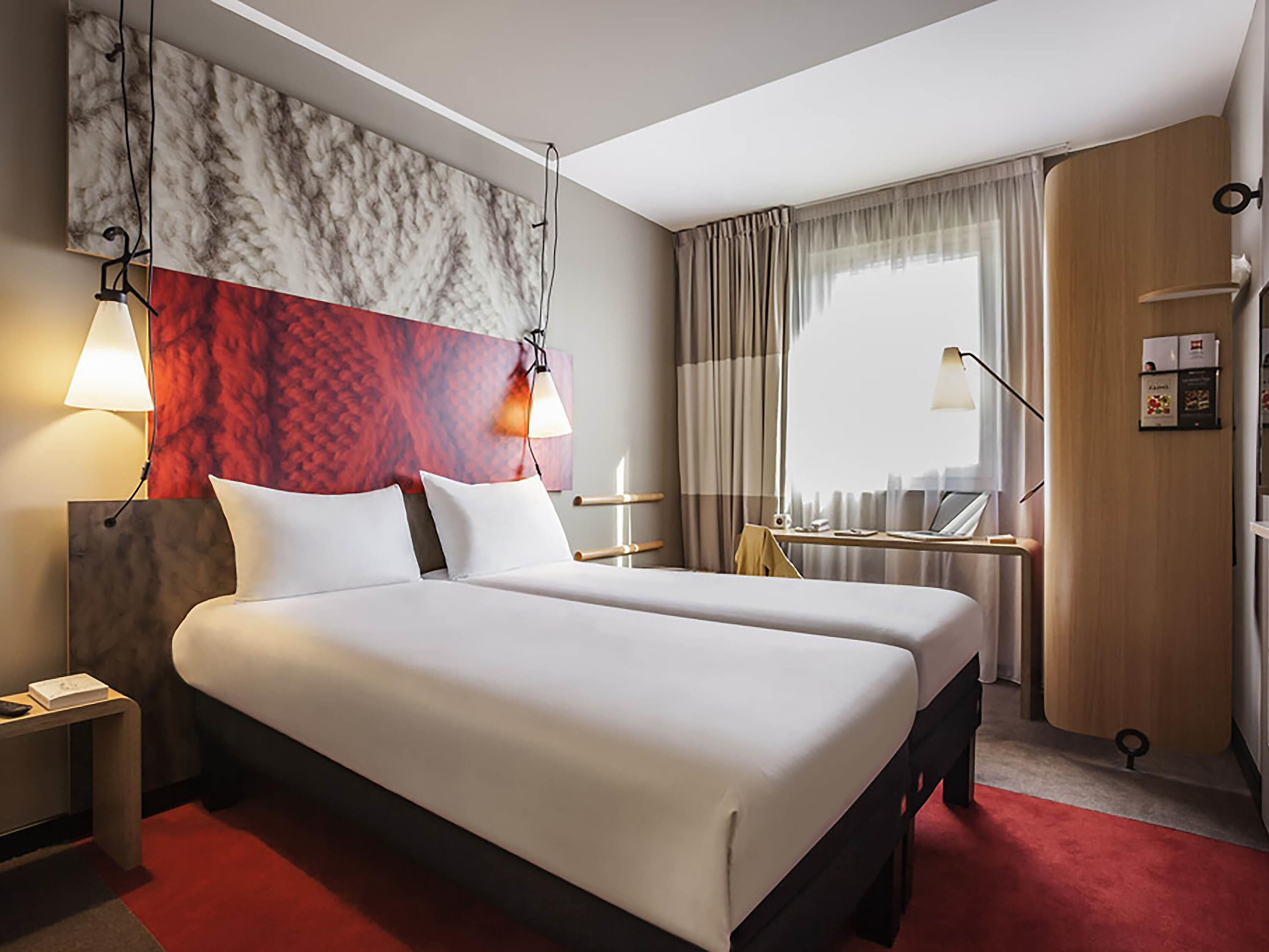 A hotel room with a bed, bedside tables, a desk, a chair, a window with curtains, and a wall with a marble-like design.