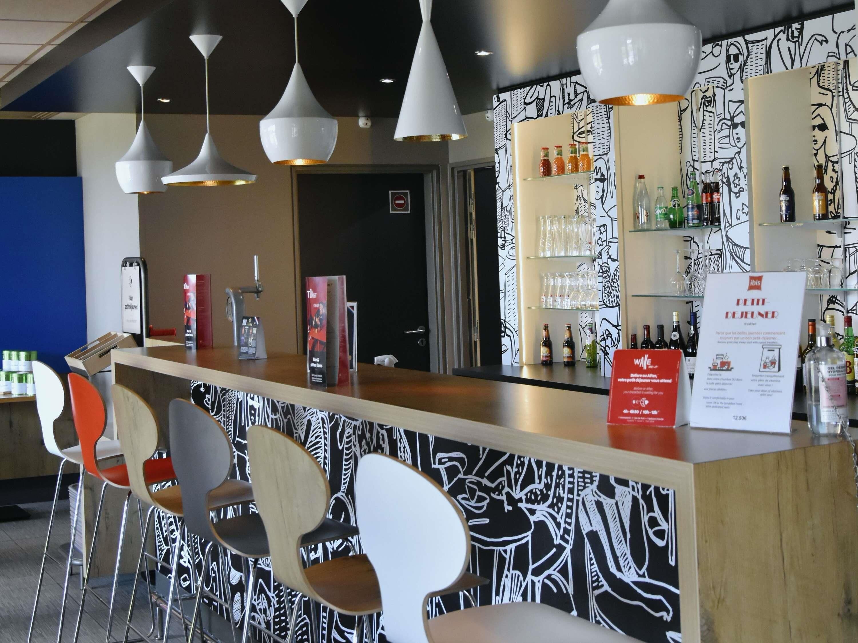 Un espace bar avec un comptoir, des chaises, des luminaires suspendus et un mur orné d’un motif noir et blanc.