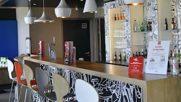 Un espace bar avec un comptoir, des chaises, des luminaires suspendus et un mur orné d’un motif noir et blanc.