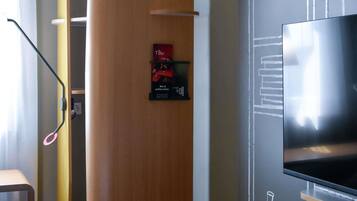 A modern hotel room with a large flat-screen TV mounted on the wall, a wooden door, and a small poster advertising a bar and restaurant.