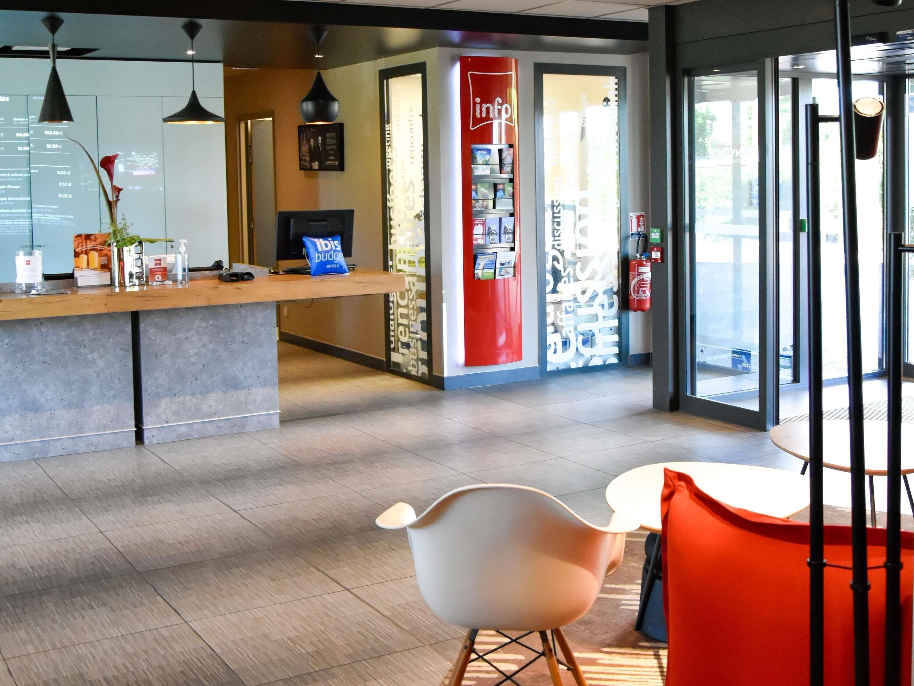 Un hall d’hôtel comprenant un comptoir d’accueil, un espace salon avec des fauteuils et une grande fenêtre donnant sur l’extérieur.