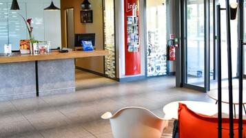 Un hall d’hôtel comprenant un comptoir d’accueil, un espace salon avec des fauteuils et une grande fenêtre donnant sur l’extérieur.